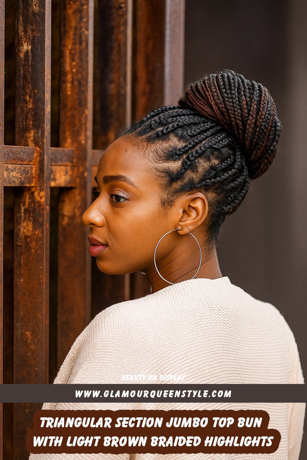 Woman wearing a large top bun made of neatly braided hair from triangular sections with light brown highlights; styled with hoop earrings and sophisticated outfit.