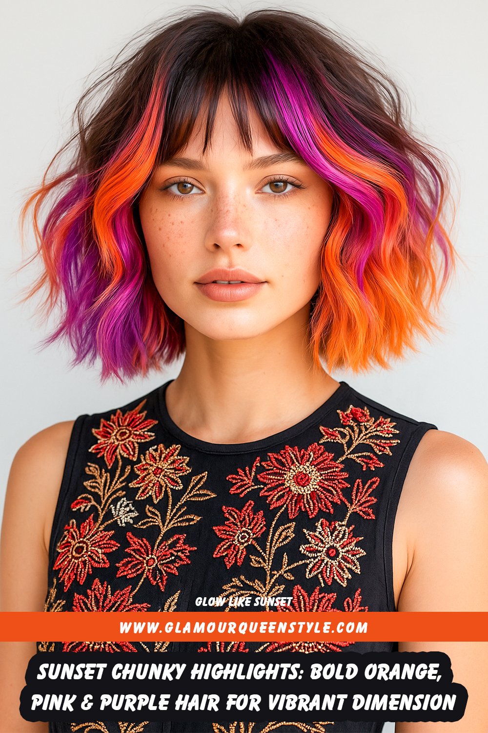 Medium-length hair styled in loose waves featuring chunky orange, pink, and purple highlights on a dark base; complemented by luminous makeup and a flowy pastel dress.
