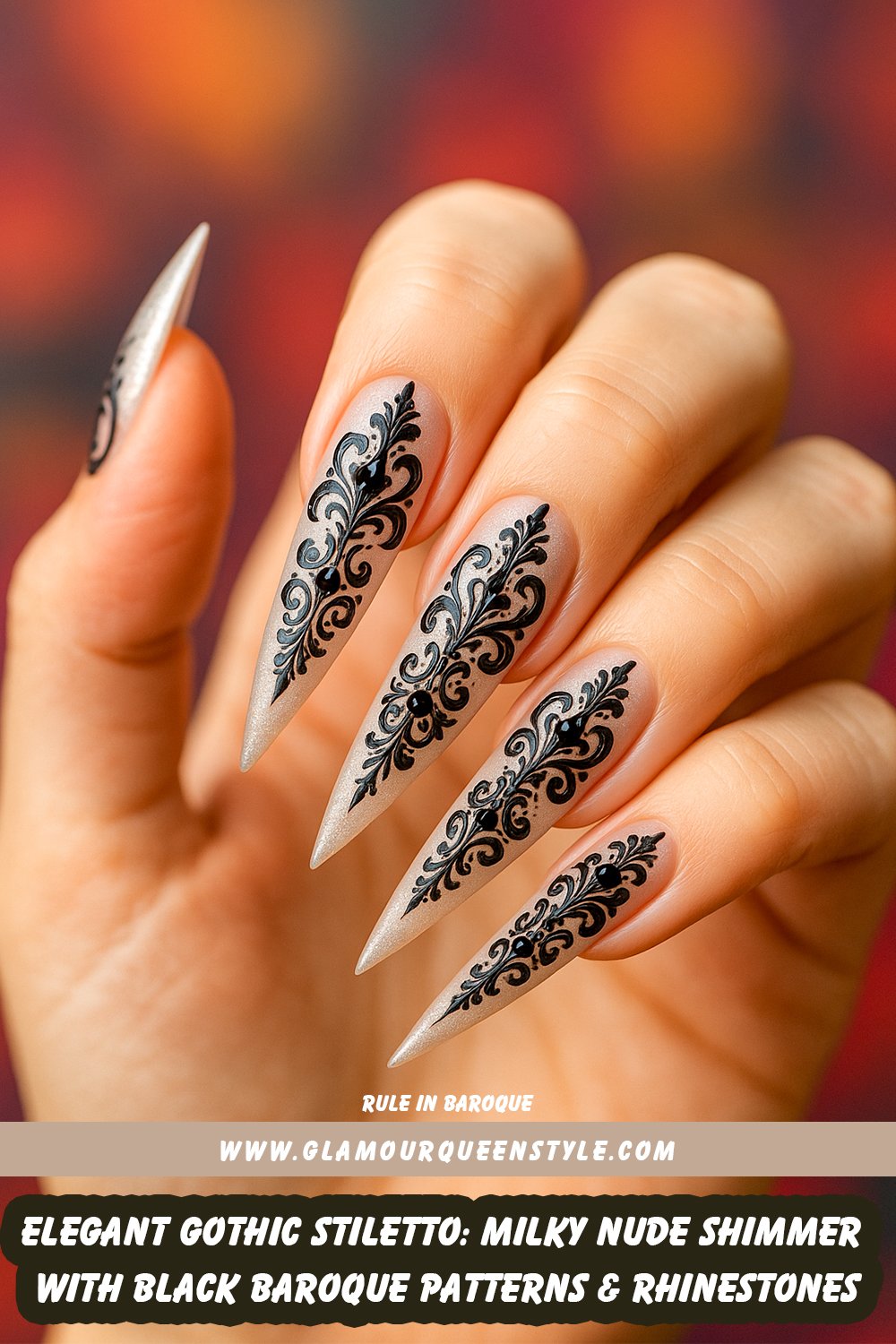 Long pointed stiletto nails in a luminous milky nude shade matched to skin tone, featuring shimmery finish; each decorated with central ornate black baroque patterns and small sparkling black rhinestones.